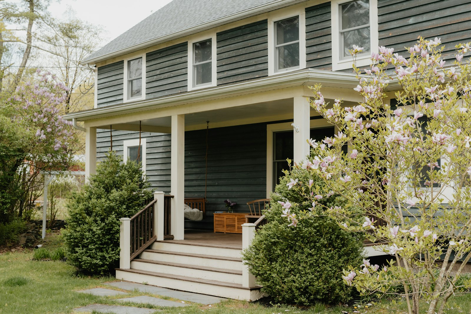 A gray two-story house with a front porch and steps to the door